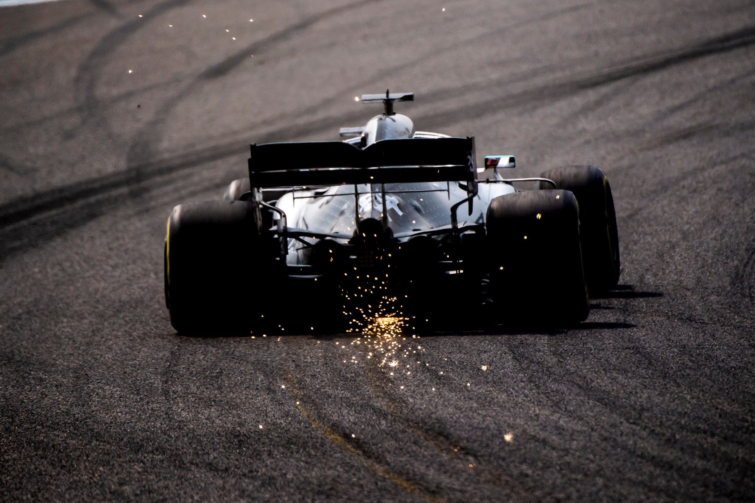 Rear view of a Formula 1 racing car speeding down a racetrack throwing intense bright yellow sparks from its floorboard.