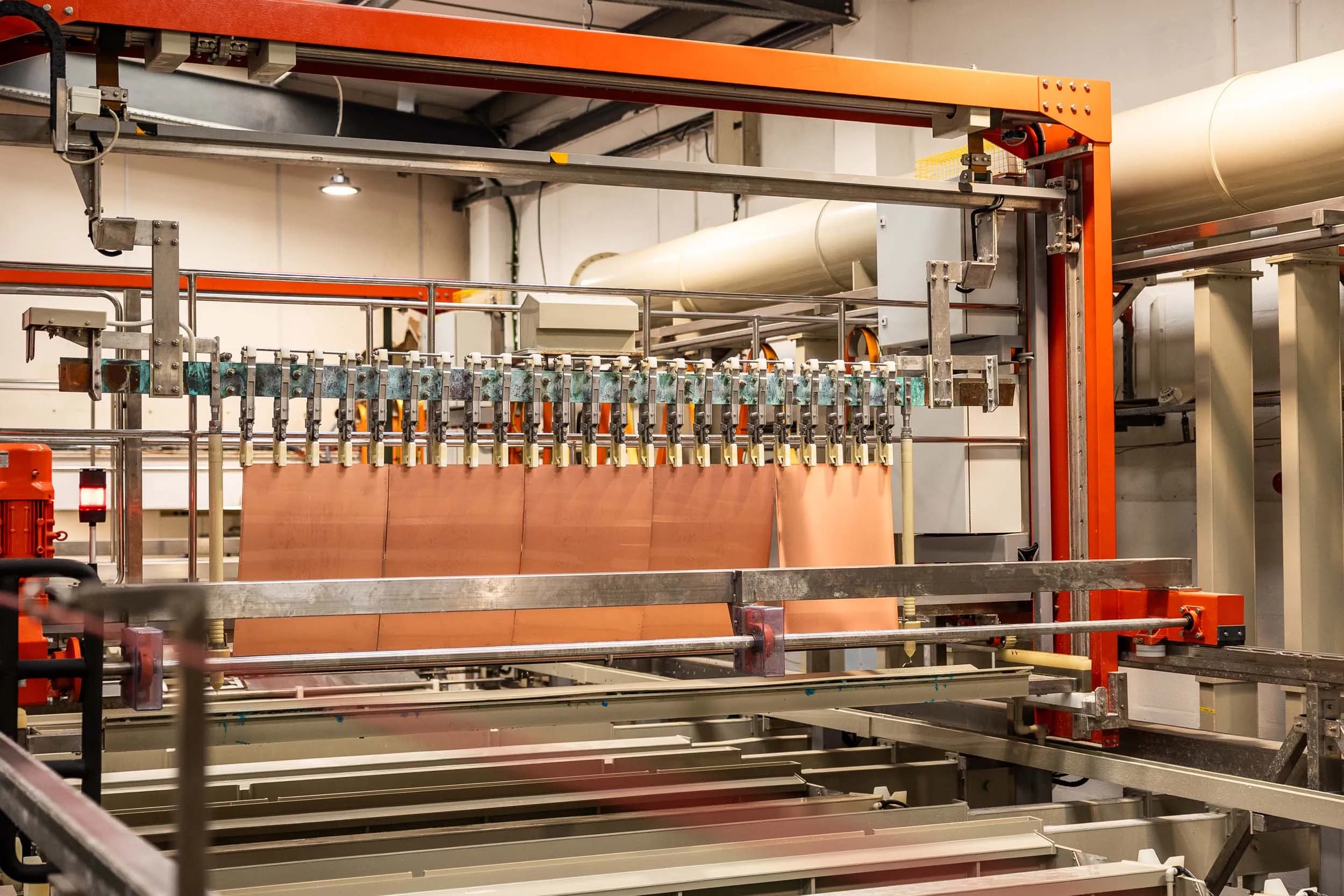 Front angle view of an automated plating gantry system moving copper sheets along chemical tanks.