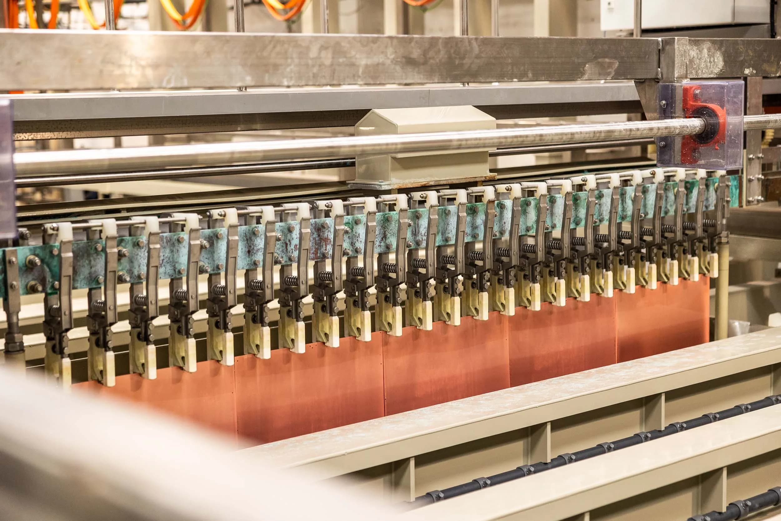 Technical close-up view of heavy-duty electroplating contact clamps and conductive busbars along a processing track.