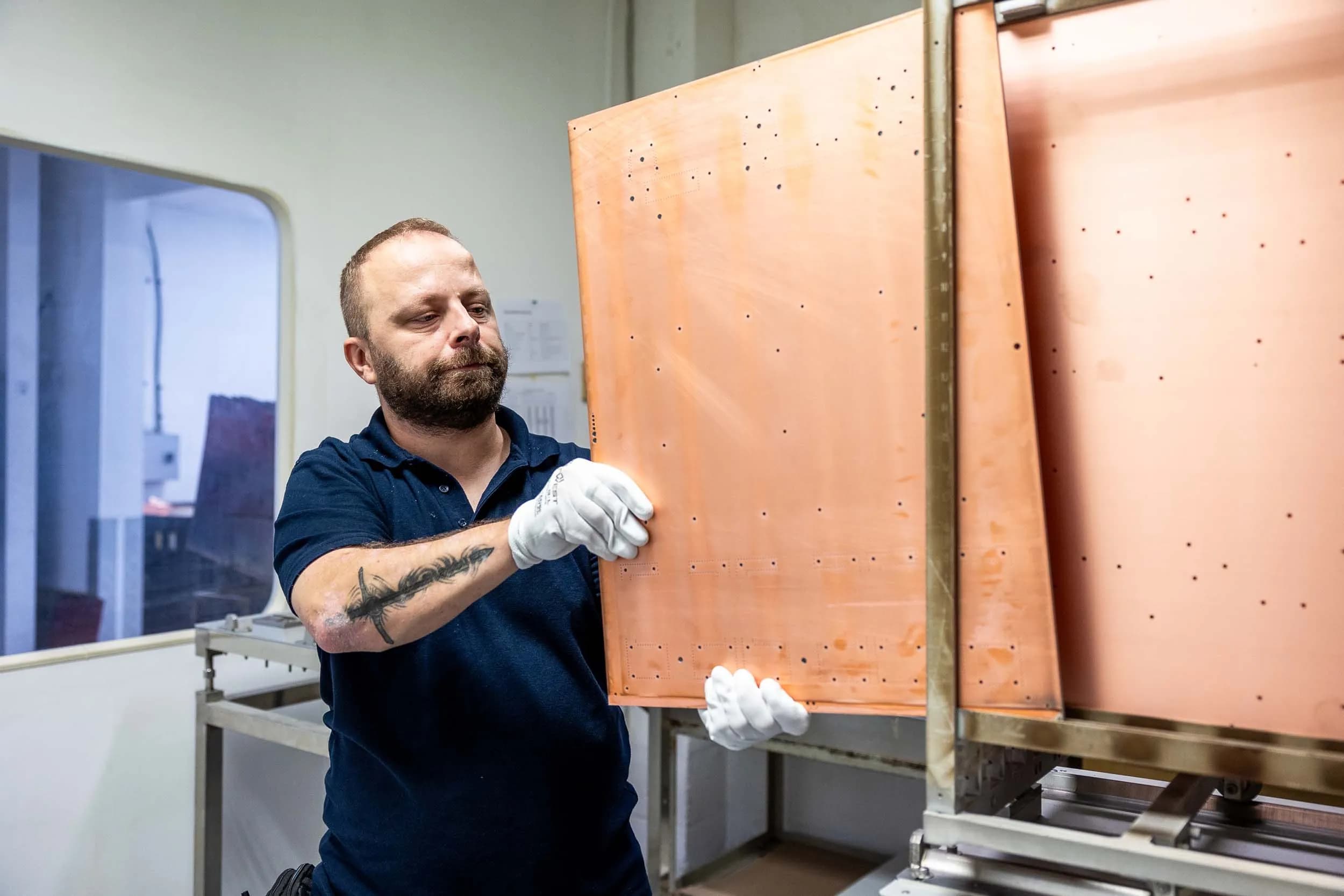 An Exception PCB technician in white gloves loading a large bare copper-clad laminate panel into a vertical thermal rack prior to pre-lamination baking.