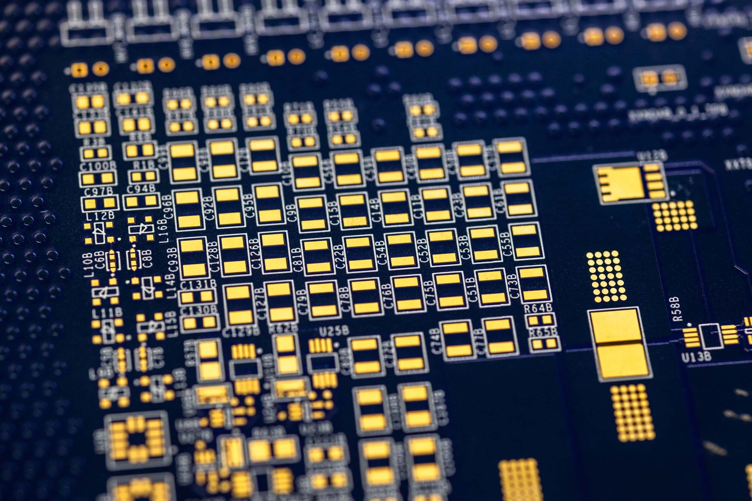 Macro view of a dark, high-density PCB showing precise gold pad layouts and trace routing.