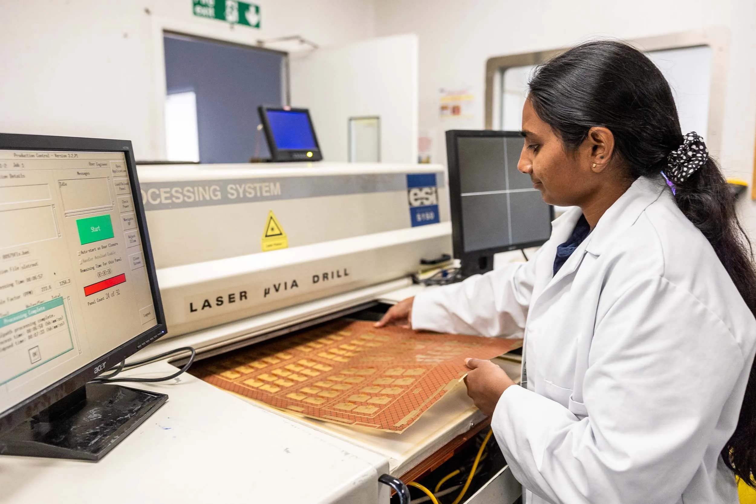 Exception PCB operator loading a flexible printed circuit board panel into an ESI laser micro via drill processing system.