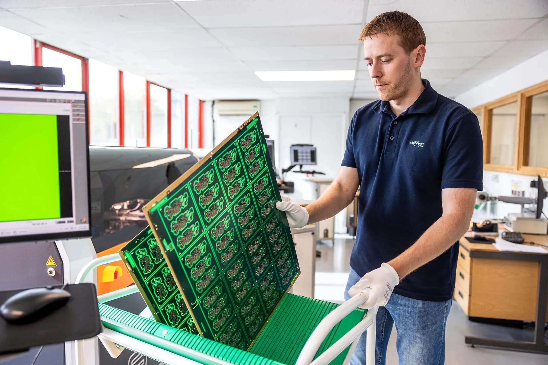 An Exception PCB technician storing green circuit board panels into a protective green slot rack cart.
