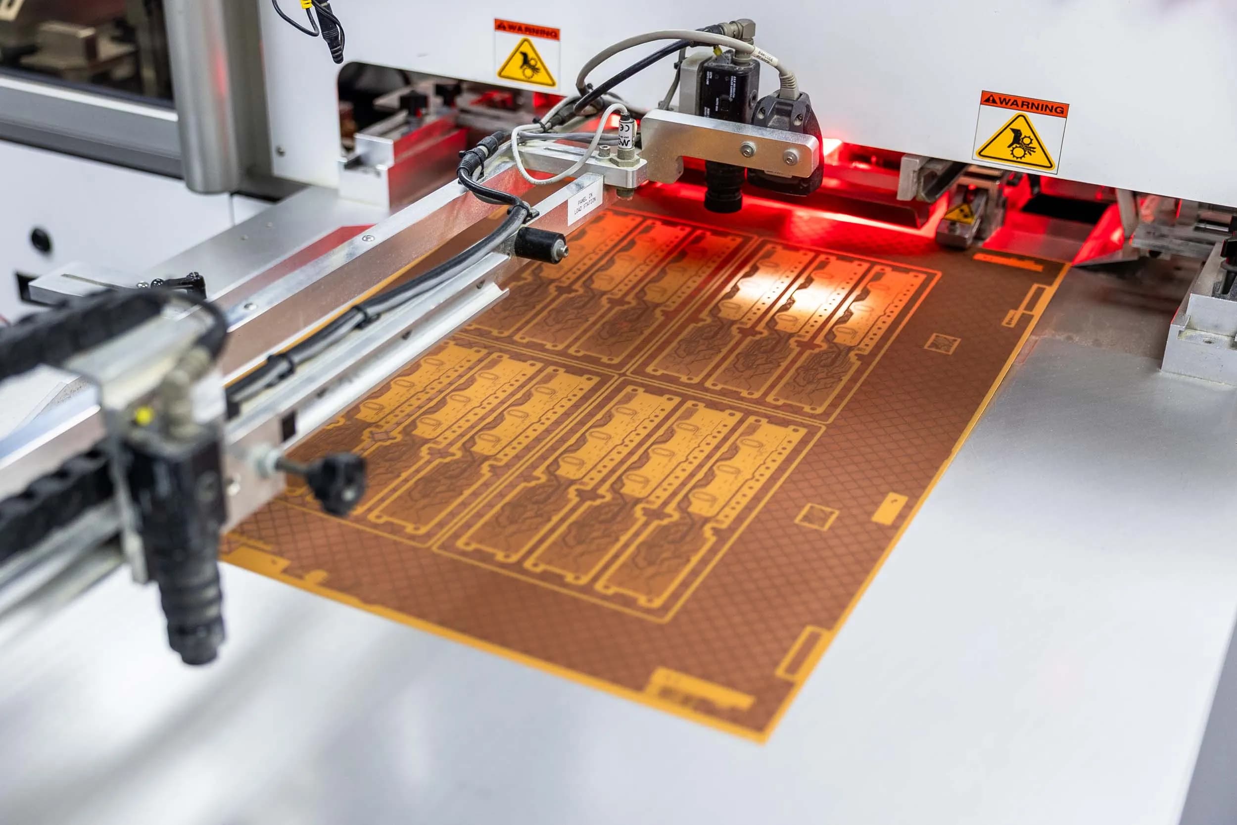 Close-up of a brown flexible circuit layer being scanned by optical camera alignment heads under red illumination.