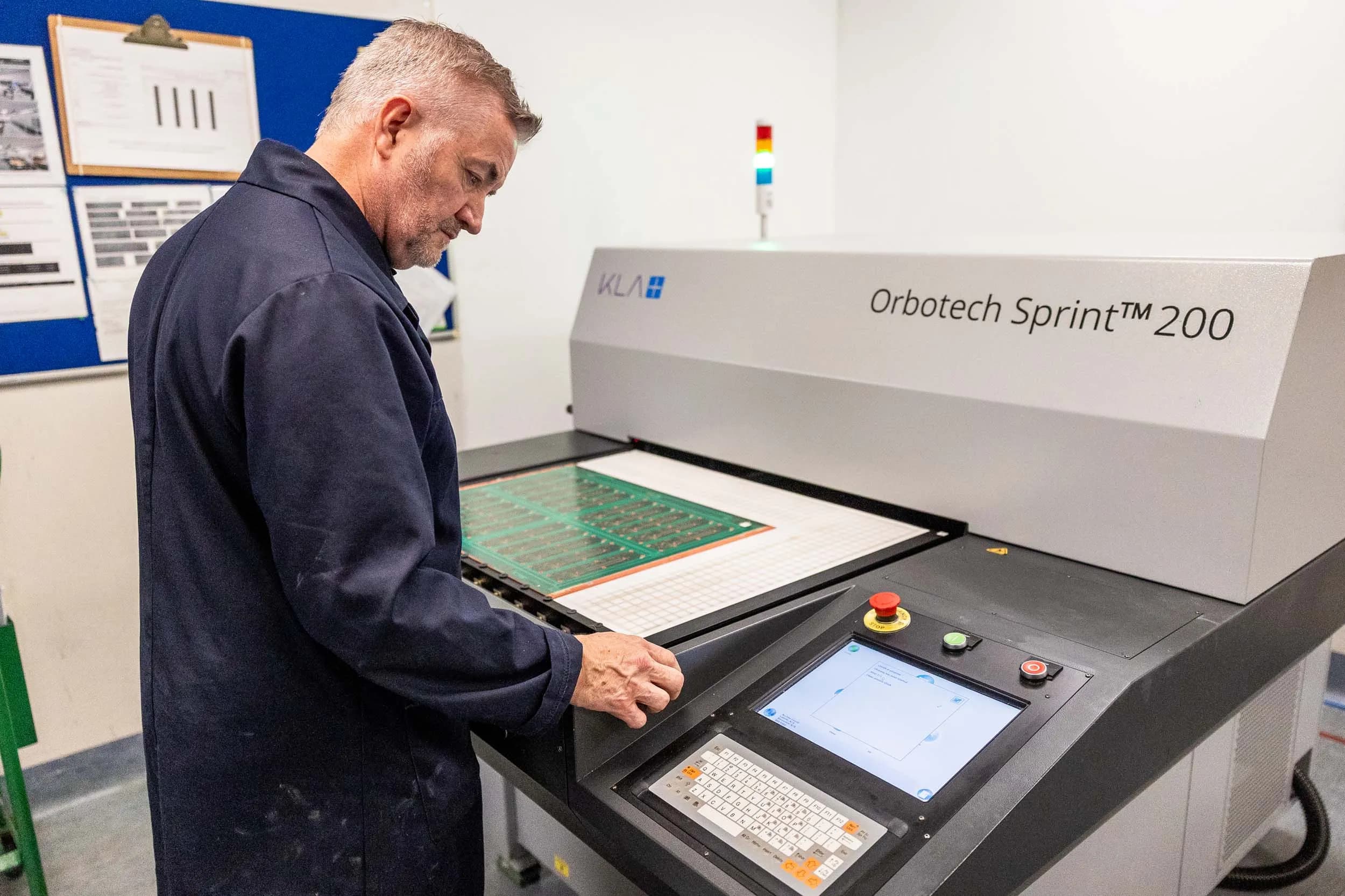 An Exception PCB technician operating an Orbotech Sprint 200 automated optical inspection machine, with a green circuit board panel loaded on the scanning bed.