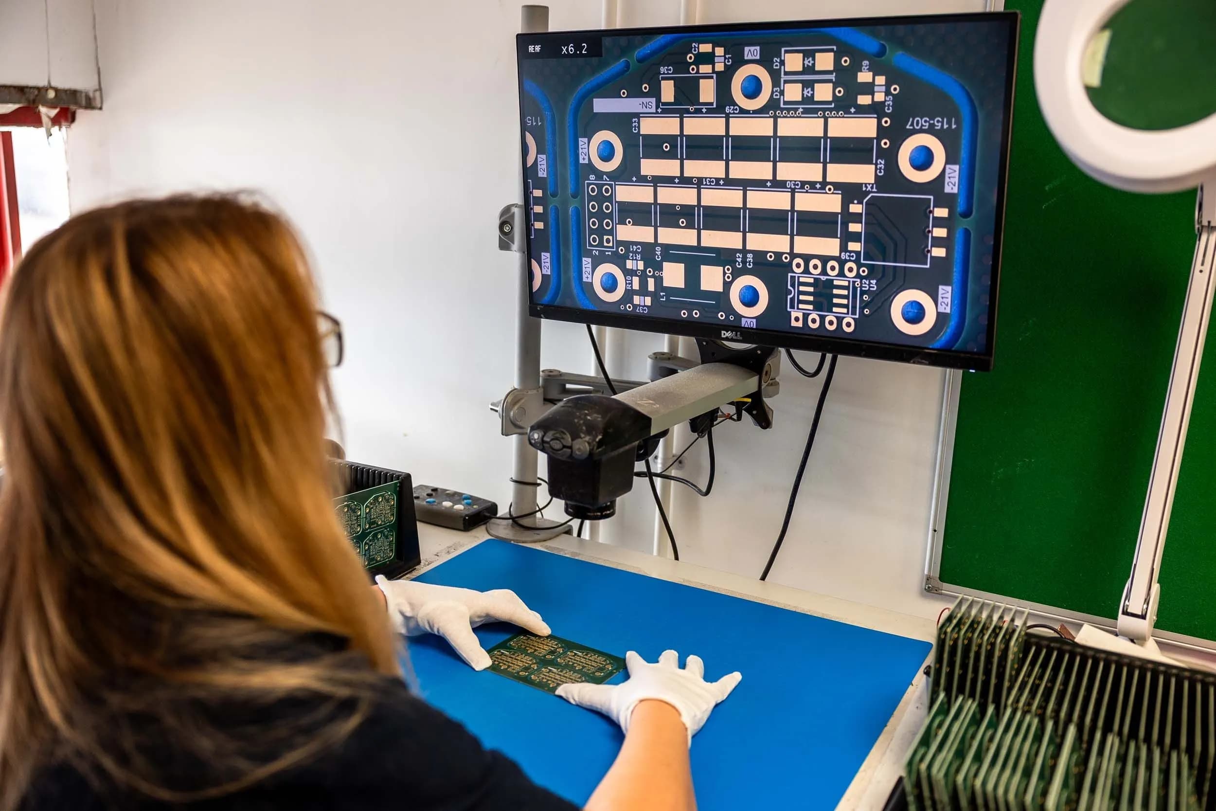 Exception PCB technician inspecting a printed circuit board using magnified screen inspection equipment.