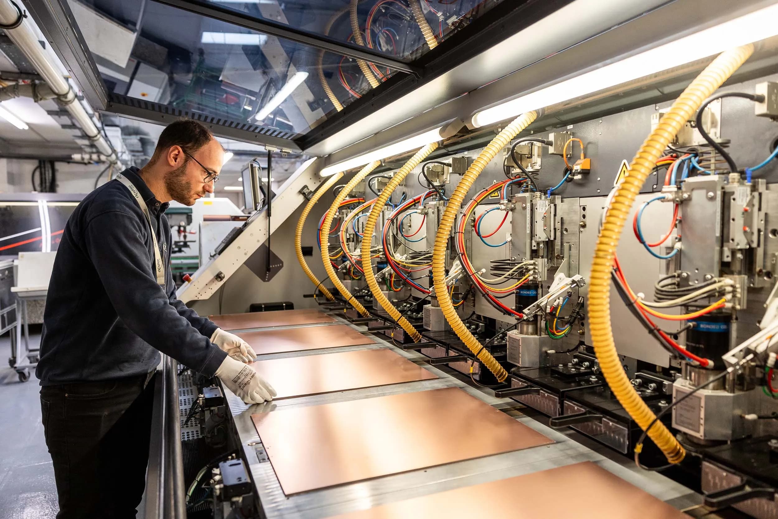 An Exception PCB technician loading copper production panels into a multi-station Schmoll CNC drilling machine.
