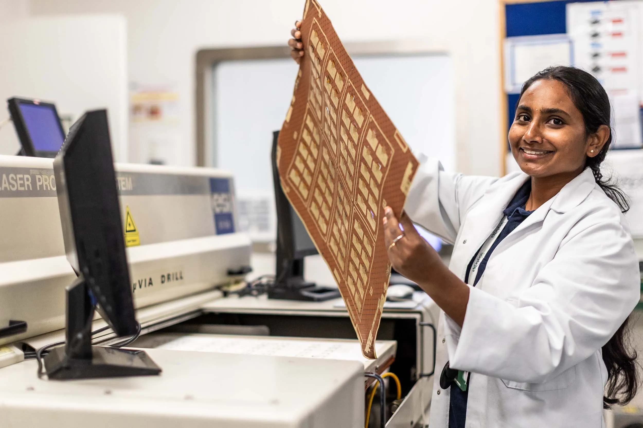 Exception PCB technician holding a flexible printed circuit board panel beside laser processing equipment.