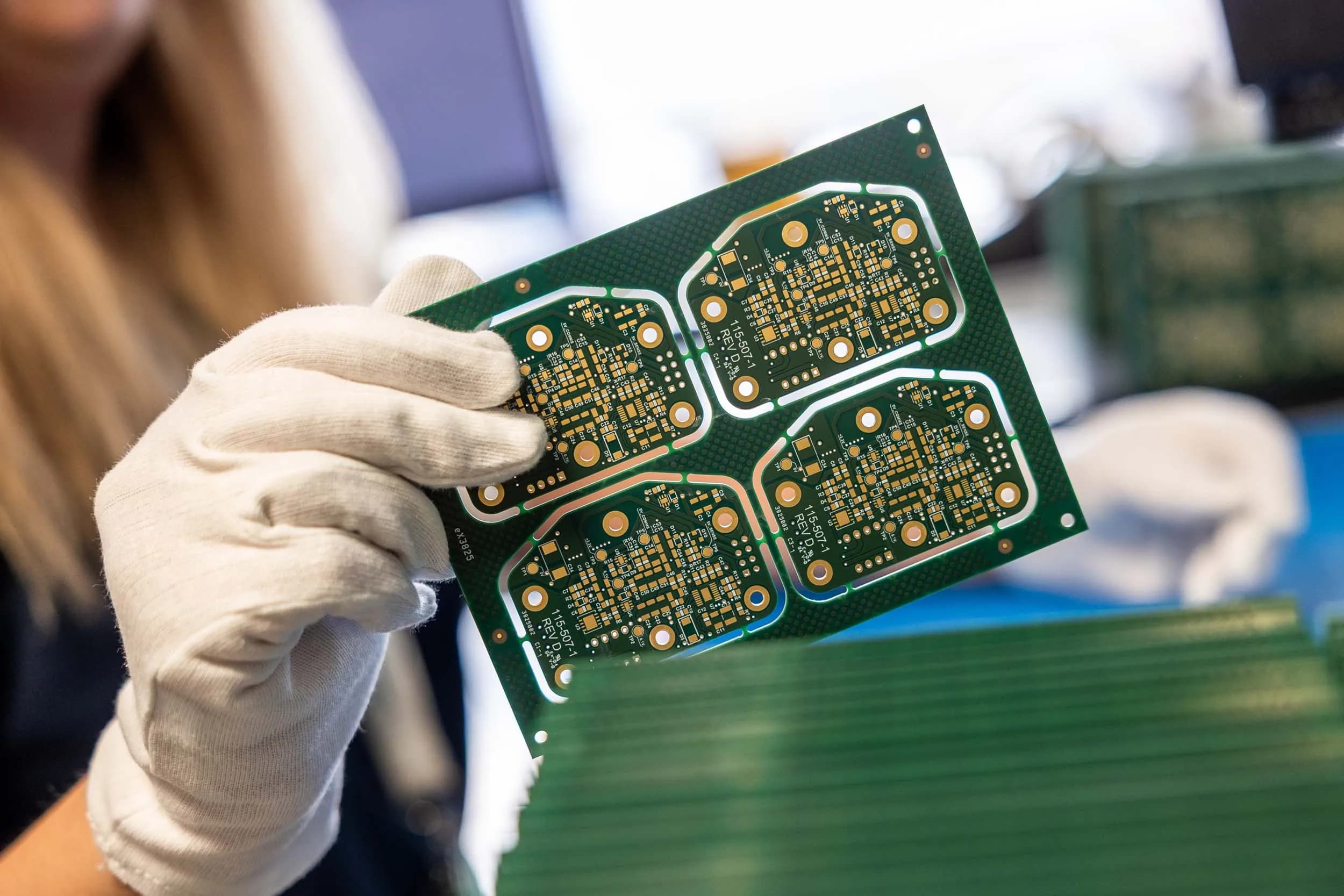 Exception PCB technician in a white glove holding a green printed circuit board panel with four individual circuits.