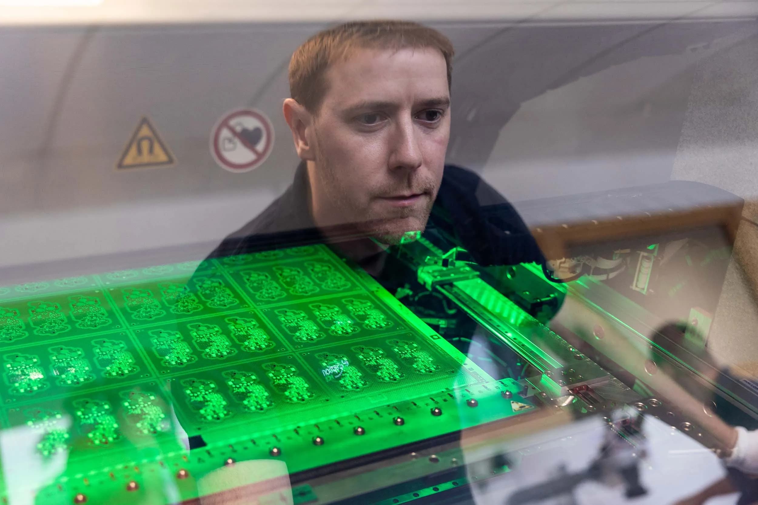 An Exception PCB technician looking through a protective glass window at an illuminated circuit board panel.