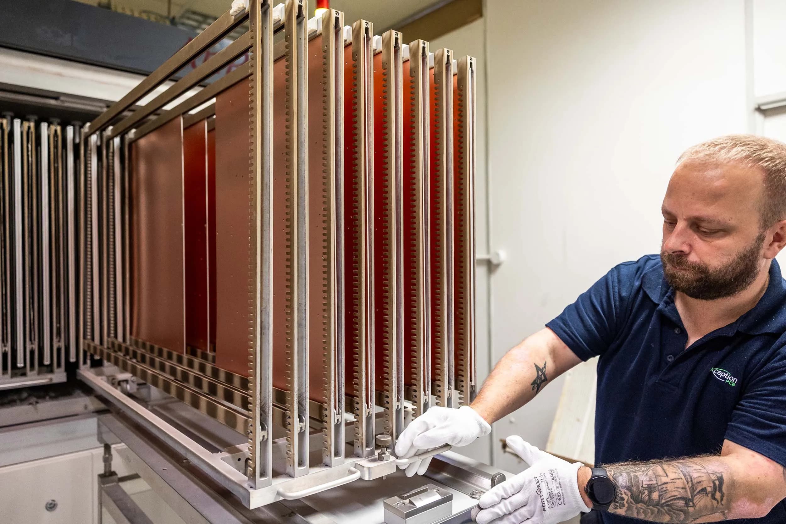 An Exception PCB technician in protective gear moving a vertical storage rack of production panels into an AnPT thermal curing oven.