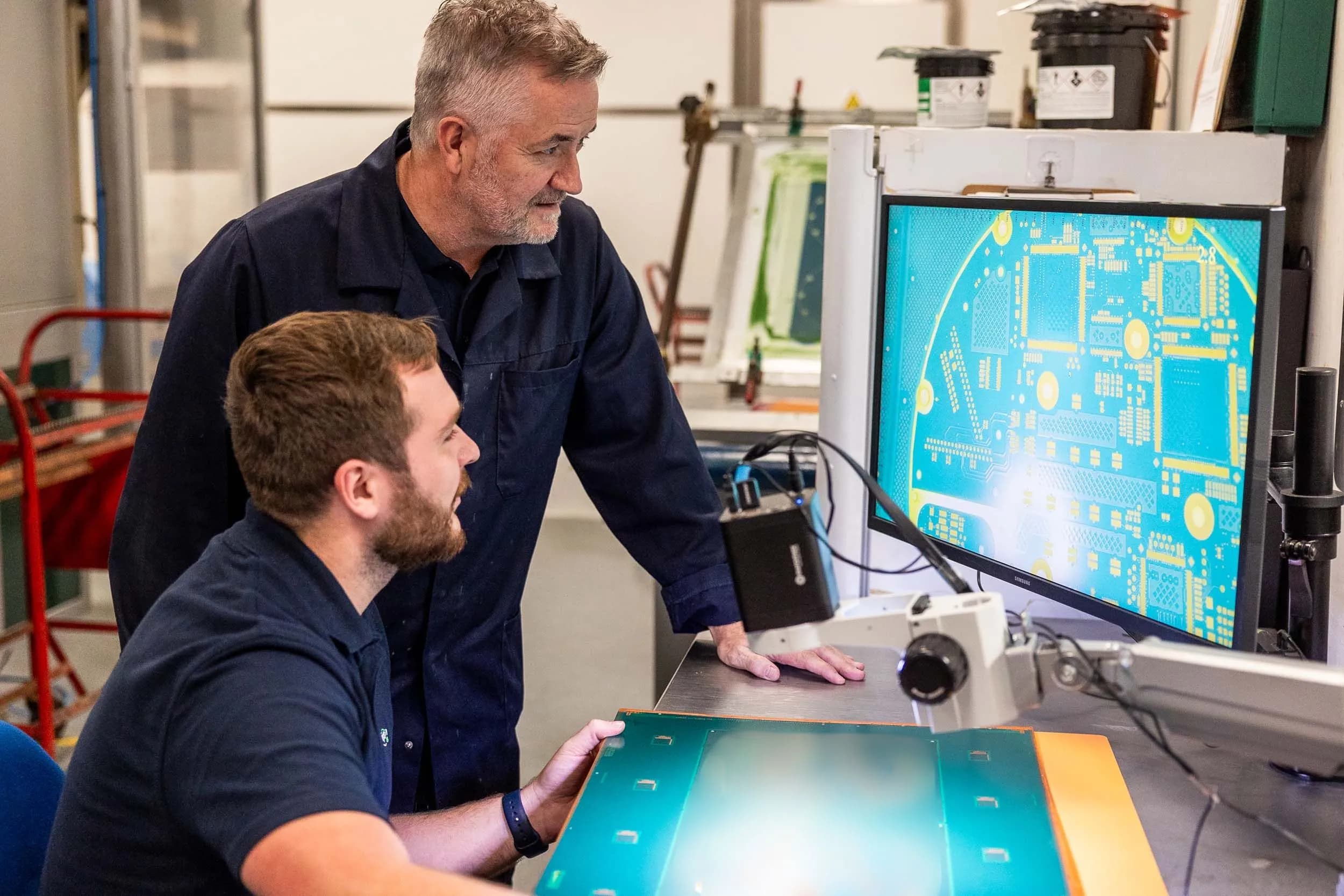 Exception PCB technicians collaborating at a digital microscope inspection workstation.