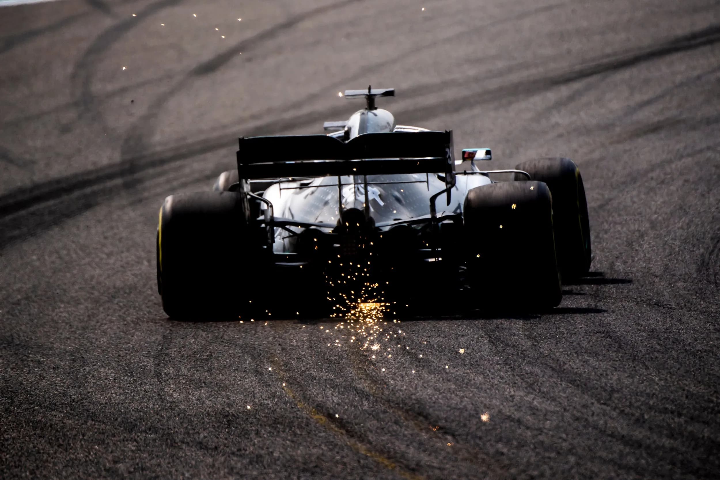 Rear view of a Formula 1 racing car speeding down a racetrack throwing intense bright yellow sparks from its floorboard.